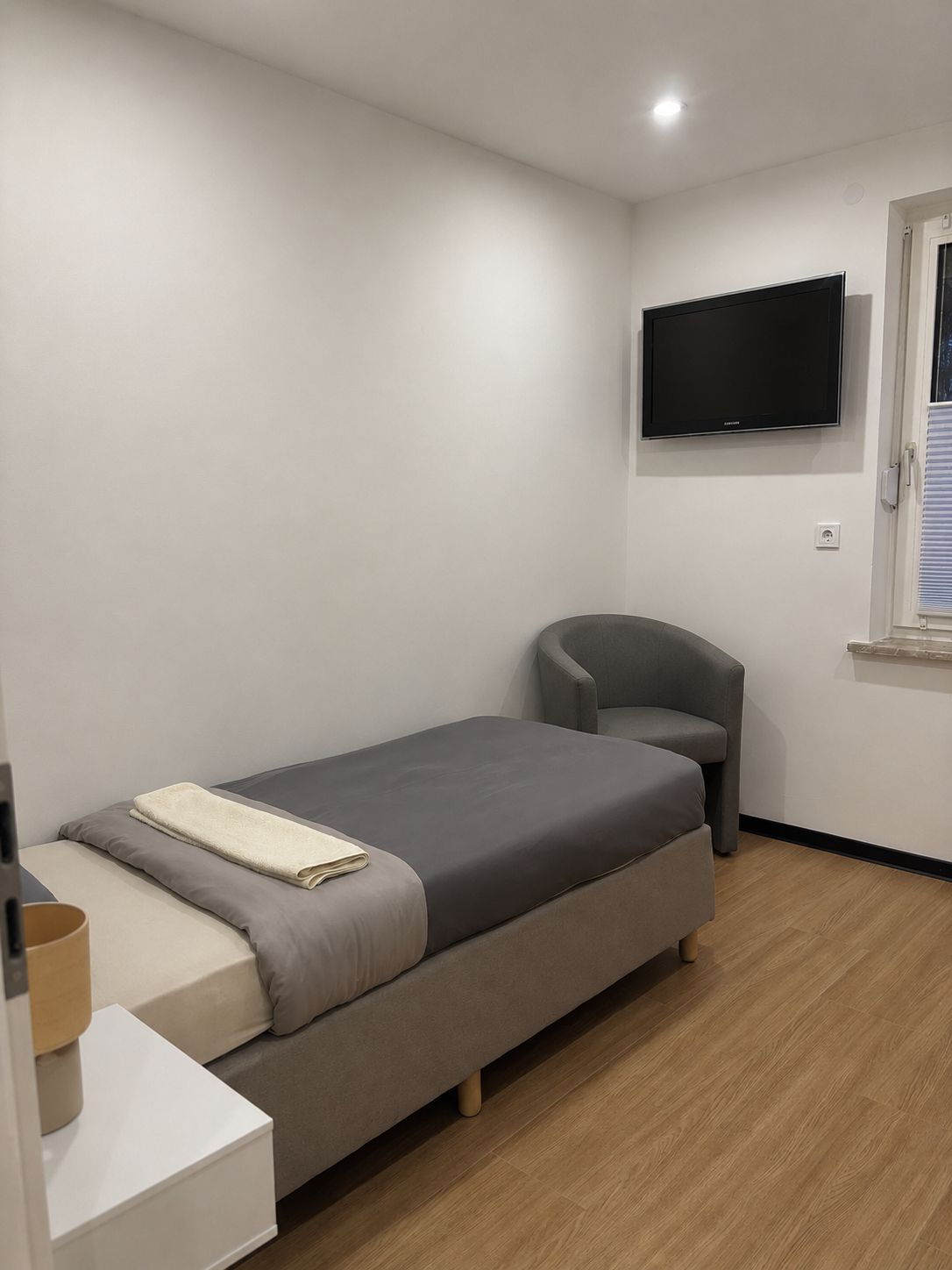 A bedroom with a bed, a chair, a television, and a window.