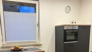Keittiössä on sisäänrakennettu uuni, seinällä oleva kello ja ikkunassa sälekaihtimet.