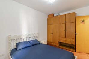 A bedroom with a bed, wooden wardrobe, and a small plant. - Apto p 6 Pessoas a 400m da Praia das Pitangueiras (Guarujá)