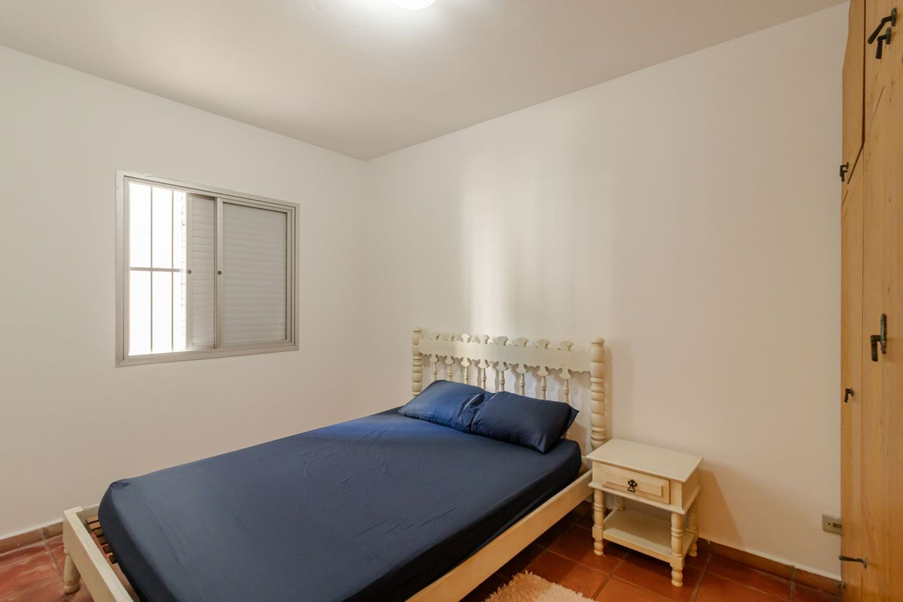 Un dormitorio con cama, mesita de noche, ventana y armario.