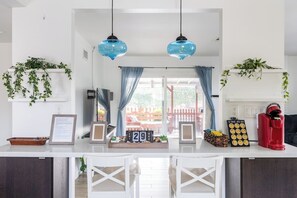 A kitchen with a white countertop, two hanging blue pendant lights, a red coffee maker, and a calendar displaying the date. - Near Disneyland | Game Room | Private Backyard (Fullerton)