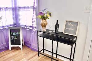 A room with a black console table, a vase with flowers, a wine bottle, and a welcome sign. - Pet friendly Huge yard, bikes Pool Table (Fullerton)