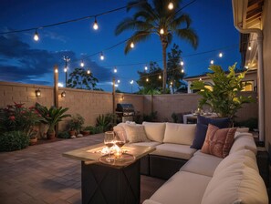 An outdoor patio with a sofa, a table with glasses, string lights, a grill, and potted plants. - Pool Table Fire Pit Spacious Disney Retreat (Placentia)