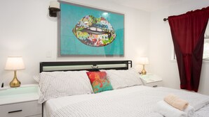 Een slaapkamer met een bed, twee nachtkastjes, een wanddecoratie en een raam met gordijnen.