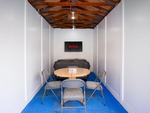A room with a blue floor, a round table with chairs, a sofa, and a wall-mounted TV displaying 'NETFLIX'. - Private 1BR w/ Yard & Workspace | Simi Valley (Simi Valley)