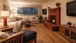 A living room with a sofa, a coffee table, a fireplace, a TV, and a window with blinds.