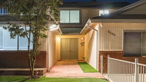 A well-lit entrance with a green door, a small tree, and a white fence.