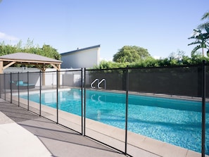 A swimming pool with a safety fence, a covered seating area, and a building in the background. - Heated Patio, 4BR Oasis w Pool & Pool Table (Tustin)
