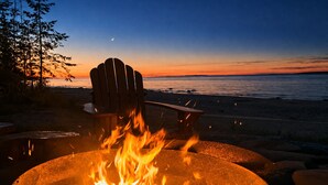 Nuotiopaikka, jossa on tuoli ja josta avautuu näkymä merelle auringonlaskun aikaan.