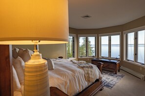 A bedroom with a large bed, a desk, and a view of the water. - Lake Huron Beach House 10 minutes from Mackinaw City, Kayaks, Gym, Amazing Views (Cheboygan)