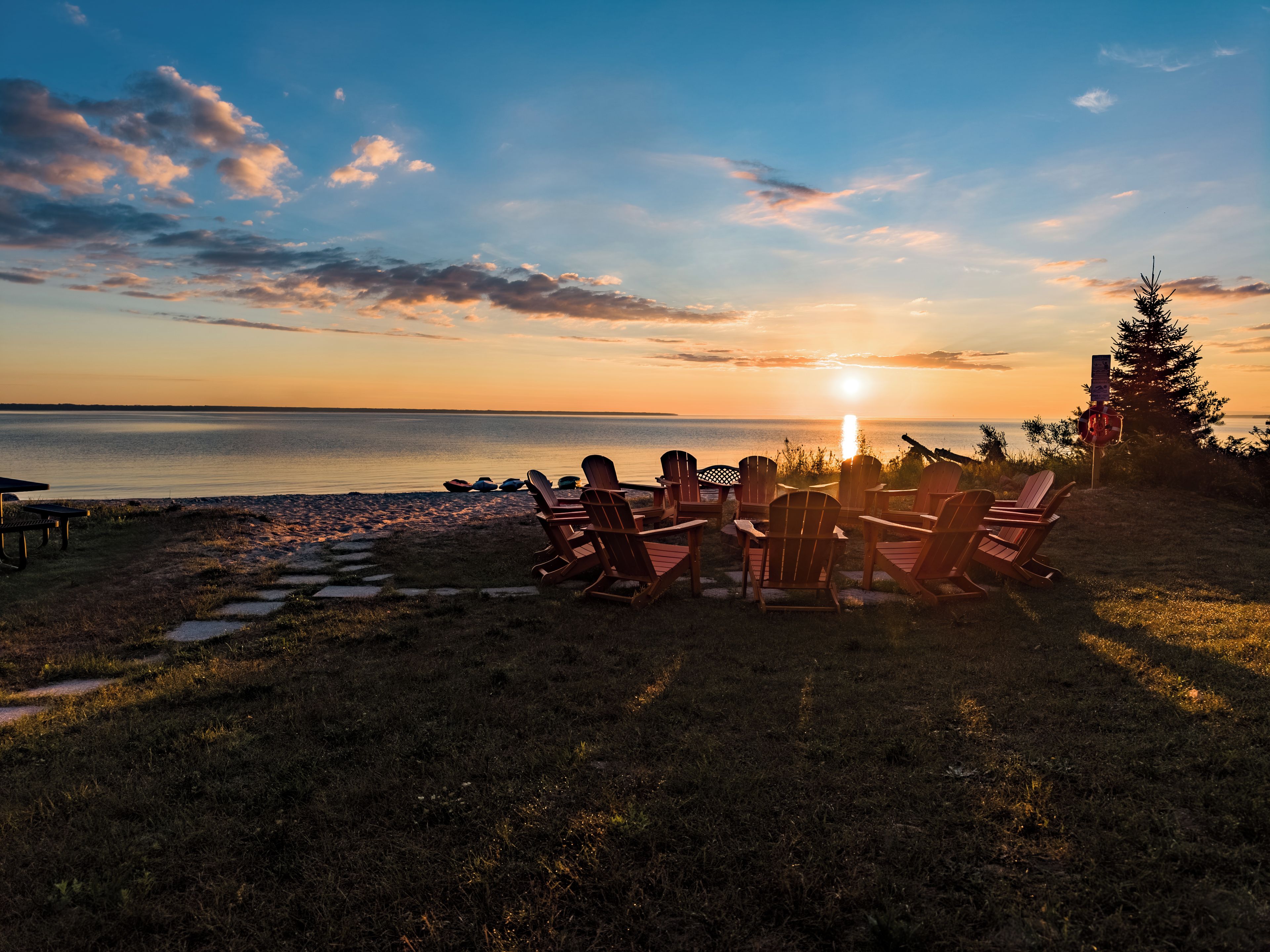 A sunset view with chairs facing the water, a small table, and a path leading to the beach.