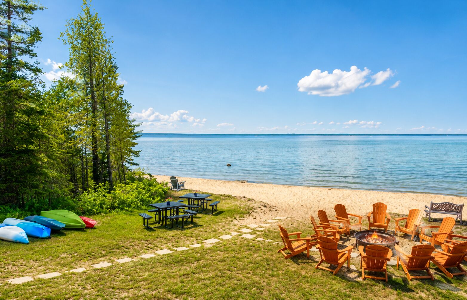 A lakeside outdoor seating area with picnic tables and Adirondack chairs, surrounded by greenery and a view of the lake.