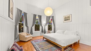 A bedroom with a bed, a chair, a rug, and a window with curtains. - Ocean View, Hot Tub, Sauna, Beach Bikes + More (Ventura)