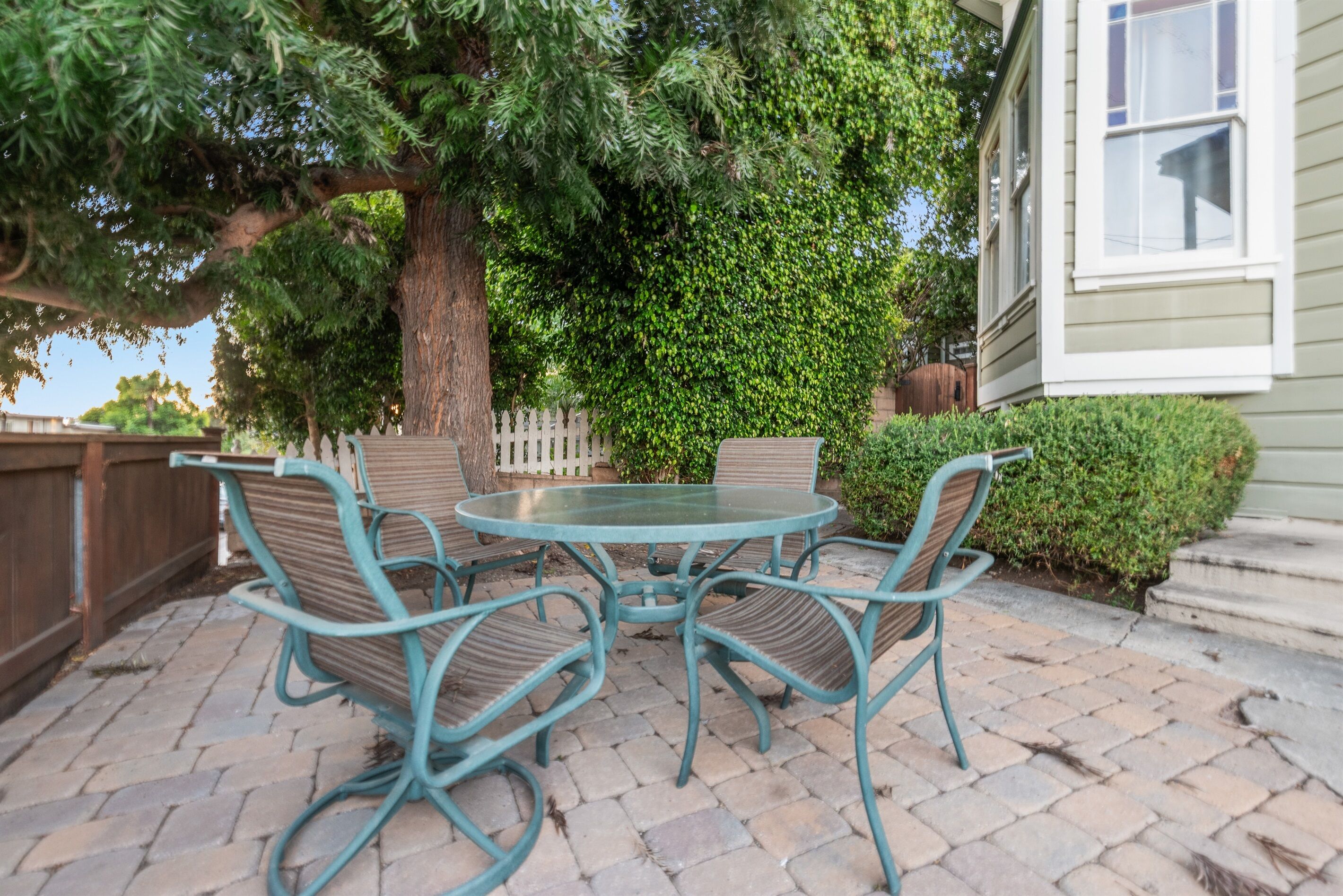 A patio with a round table and four chairs, surrounded by a wooden fence and a large tree.