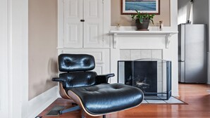 A modern living room with a leather chair, a fireplace, a white door, and a kitchen area with a refrigerator. - Ocean View, Hot Tub, Sauna, Beach Bikes + More (Ventura)