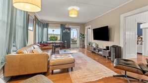 A spacious living room with a sofa, ottoman, and a television mounted on the wall. - Ocean View, Hot Tub, Sauna, Beach Bikes + More (Ventura)