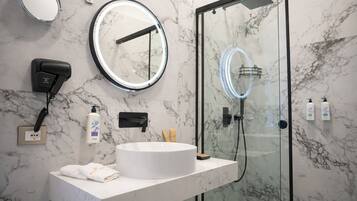 A modern bathroom with a marble sink, a round mirror, a hairdryer, and a glass-enclosed shower.
