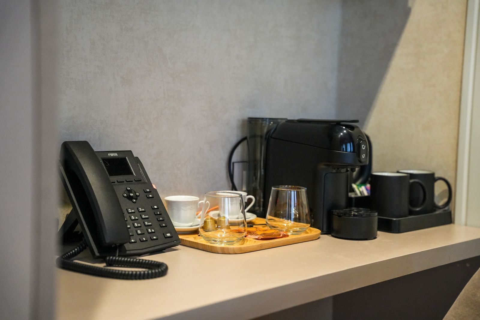 A hotel room with a telephone, coffee maker, and tea set on a counter.