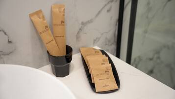 A bathroom with a marble sink, a black cup, and paper bags labeled 'Dental Kit' and 'shower cap.'