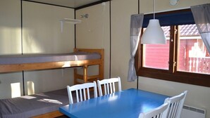 A bunk bed with a table and chairs, a hanging light fixture, and a window with curtains. - Siljansbadets Camping (Rattvik)