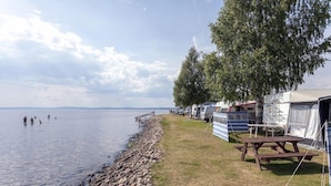 A lakeside campsite with RVs, picnic tables, and a rocky shoreline. - Siljansbadets Camping (Rattvik)