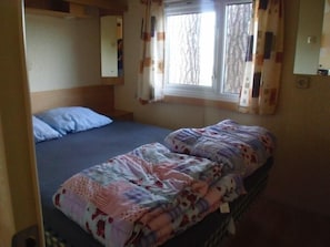 Una cama individual con una colcha estampada, una ventana con cortinas y un espejo en la pared.