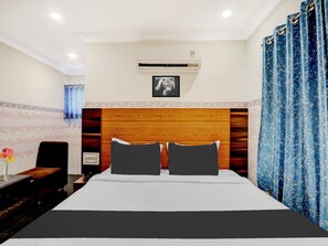 Habitación de hotel con cabecera de madera, cama con ropa de cama blanca y negra, un cuadro en la pared y cortinas azules.