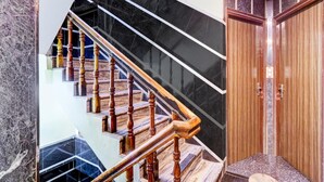 A staircase with wooden balusters and black marble steps, leading to a room with a wooden door and a security camera. - Hotel O Hanuman Pet Railway Station (Vijayawada)