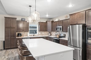 A modern kitchen with dark wood cabinets, stainless steel appliances, a large island, and pendant lighting. - On the Rocks Lodge - Sleeps 18 (Branson)