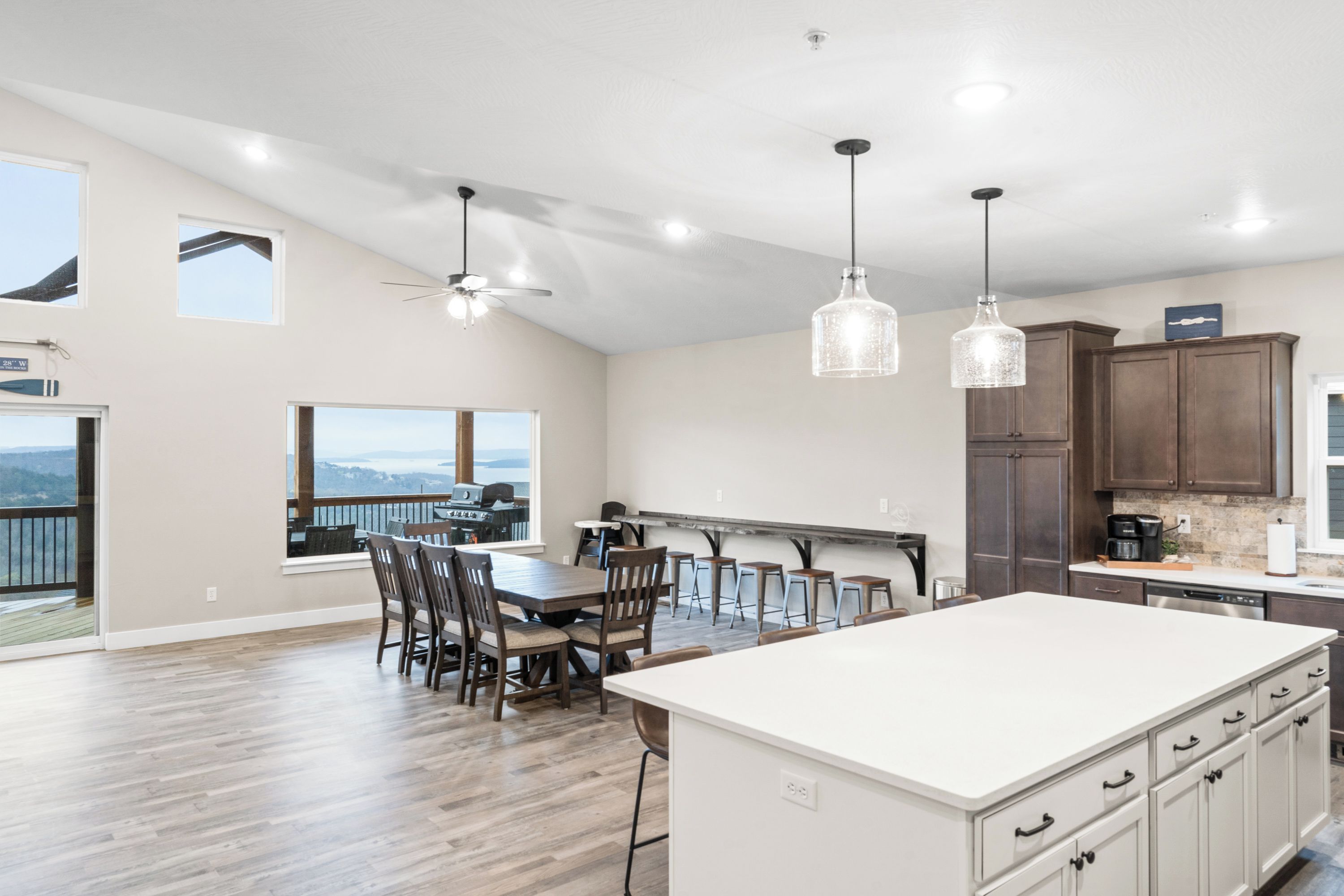 A spacious kitchen with a large island, wooden chairs, pendant lights, and a view to the outdoors.