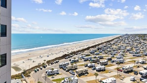 Un campeggio per camper sul lungomare, con file di camper, una spiaggia sabbiosa e l'oceano.