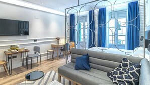 Ett modernt vardagsrum med en soffa, en matplats, en tv och ett stort fönster med gardiner.