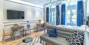 A modern living room with a sofa, a dining area, a TV, and a large window with curtains. - Victoria XVII - Studio Apartment, Sleeps 2 (Malaga)