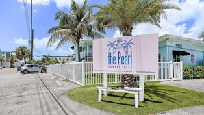 Señal que indica 'The Pearl Cabana Club', con una cerca blanca y palmeras.