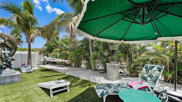 Un patio con una sombrilla verde, sillas de lounge blancas, una mesita y una escultura decorativa.