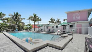 Una piscina con sillas de descanso, palmeras y un edificio con el rótulo 'The Pearl'.