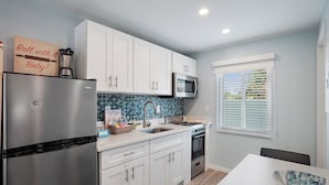 Una cocina moderna con armarios blancos, un refrigerador de acero inoxidable, un microondas y un lavamanos.