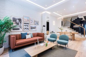 A modern living room with a white brick wall, a brown sofa, a wooden coffee table, and a staircase leading to another level. - Victoria XVI - Studio Apartment, Sleeps 2 (Malaga)