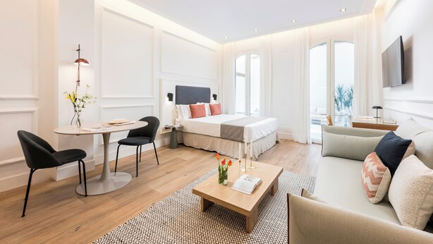 Una habitación de hotel moderna con una cama, un sofá, una mesa de comedor y un televisor.