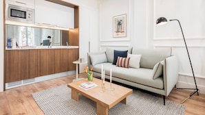 A modern living room with a sofa, a coffee table with books and candles, a kitchen area with a microwave, and a floor lamp. - Victoria XIX - Studio Apartment, Sleeps 2 (Malaga)