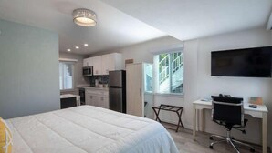 Une pièce de taille modeste comprenant un lit, un bureau, une chaise, un téléviseur et un coin cuisine.