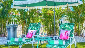 Une terrasse avec deux fauteuils de jardin verts et blancs, un parasol assorti et des palmiers en arrière-plan.