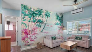 A living room with a tropical mural, two sofas, a coffee table, and a ceiling fan. - Unit 104 King Suite 1 Bed/1Bath - Partial view - The Pearl Cabana Club (St Pete Beach)
