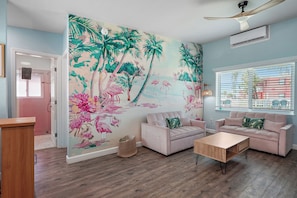 Una sala de estar con un mural tropical, dos sofás, una mesa de centro y un ventilador de techo.