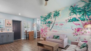 A living room with a wooden coffee table, a sofa, and a mural of tropical birds and flowers. - Unit 104 King Suite 1 Bed/1Bath - Partial view - The Pearl Cabana Club (St Pete Beach)