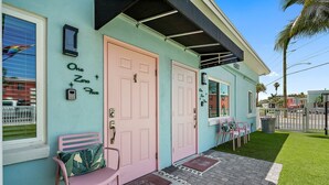 A building with two pink doors, a small bench, and a green lawn. - Unit 105 King Suite 1 Bed/1 Bath - The Pearl Cabana Club (St Pete Beach)