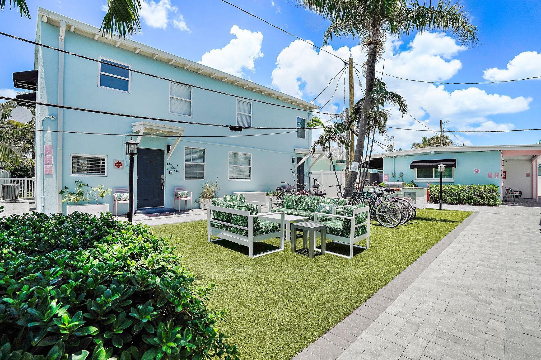 A light blue building with a flat roof, a front door, and a small porch with outdoor furniture.