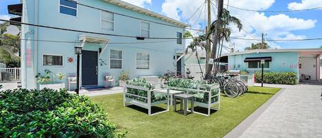 A light blue building with a flat roof, a front door, and a small porch with outdoor furniture.
