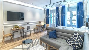 Una sala de estar moderna con un sofá, una mesita de centro y un televisor. Hay cortinas azules y un ventanal grande.