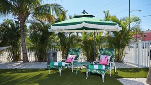 Een terras met twee groene en witte loungestoelen, een klein rond tafeltje en een groene parasol.